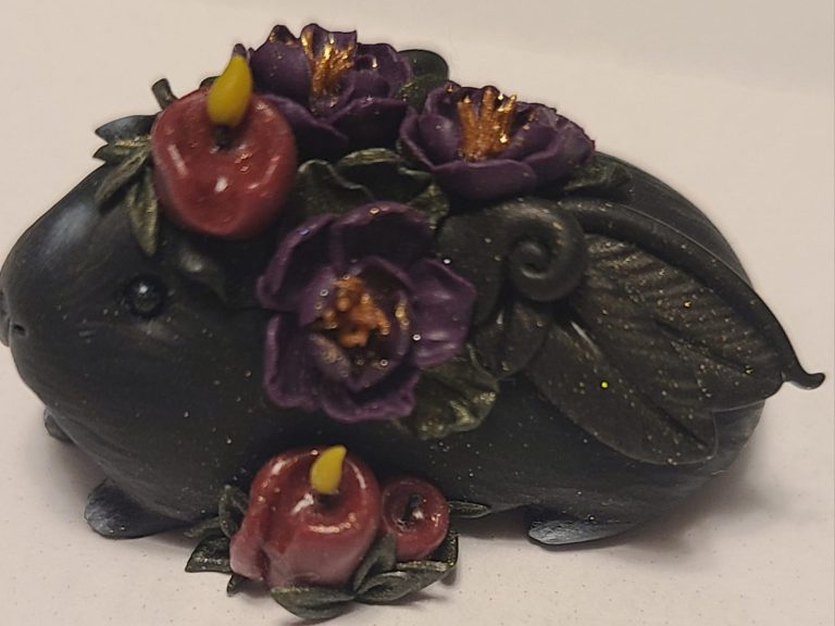 Kundenfoto von Pegaschweinchen Figur mit lila Blumen und roten Kerzen.